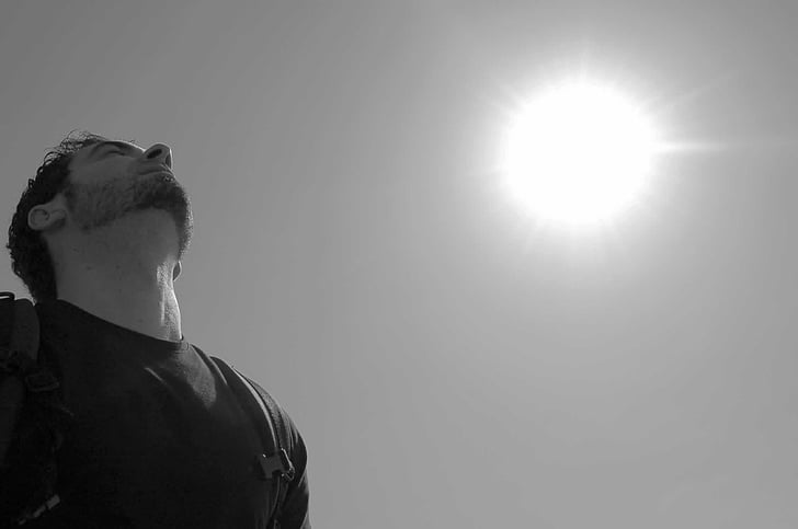 grayscale photo of man wearing t-shirt carrying backpack under sun