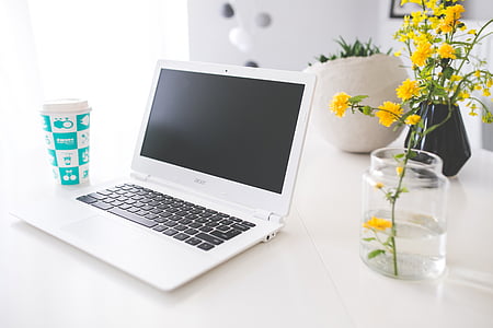 white Acer laptop beside vase of yellow cluster flower on white wooden table