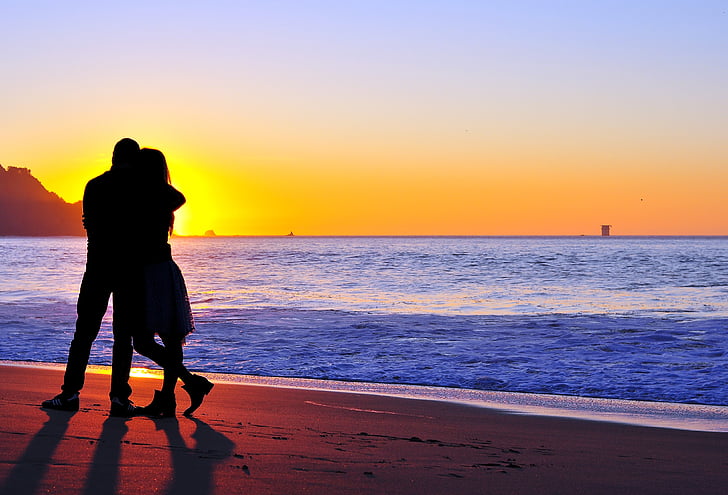 silhouette of man and woman beside body of water