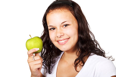 woman in white shirt holding green apple while smiling