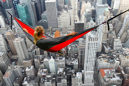 woman sitting on and red hammock overlooking high-rise buildings