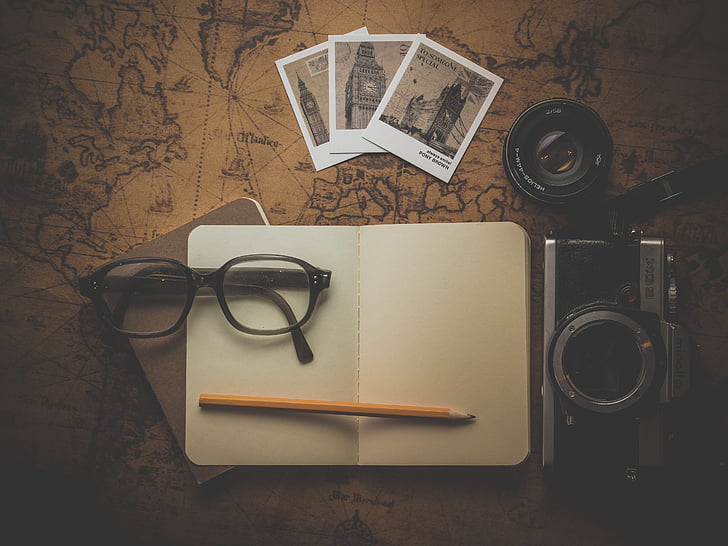 eyeglasses, pencil, planner, camera, and photos on brown map