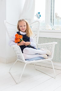 girl holds orange rose flowers while sitting on white metal armchair