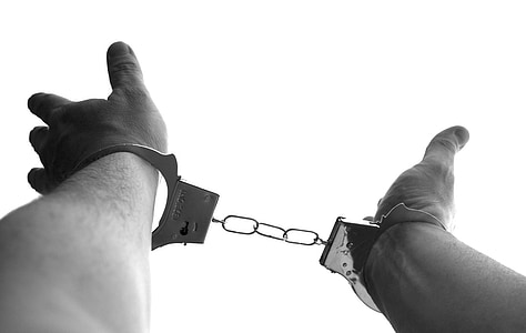 grayscale photography of person's hand with metal handcuffs