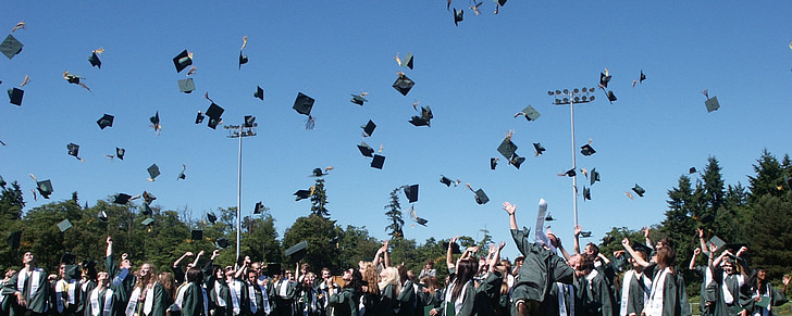 students throwing mortar boards in open field at daytime