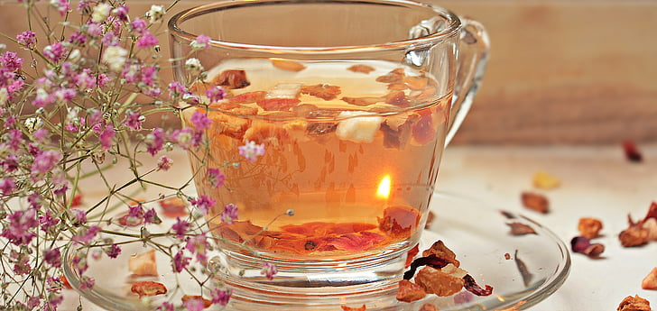 photo of filled clear glass teacup with saucer and flower petals