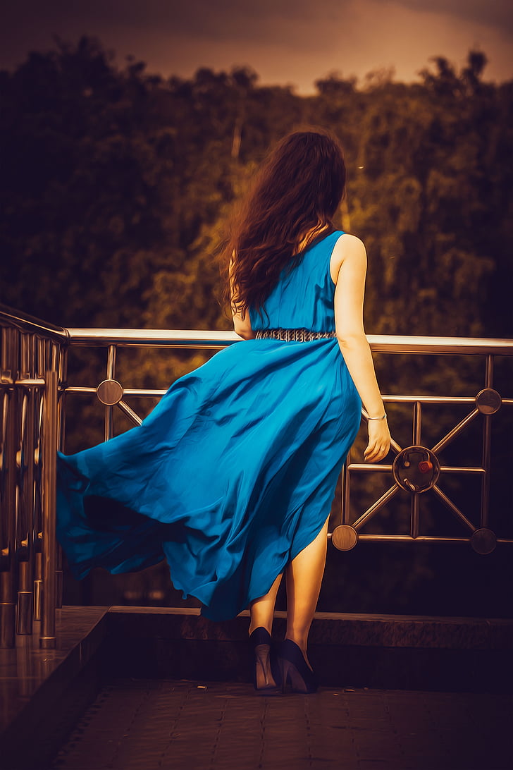 woman wearing blue sleeveless dress and black heels standing beside gray metal railings