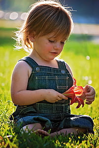girl in blue overall pants holding red lily flower