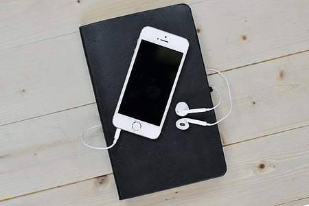 silver iPhone 5s with EarPods on top of black notebook
