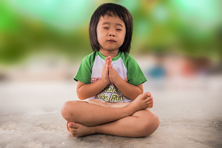 girl wearing white and green shirt sitting while praying on grey concrete floor