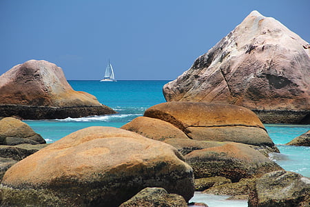brown and gray rocks in seashore with white boat in the background
