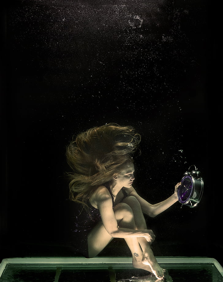 woman holding alarm clock while under the water photo