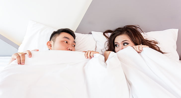 man and woman on white bed covered by white blanket