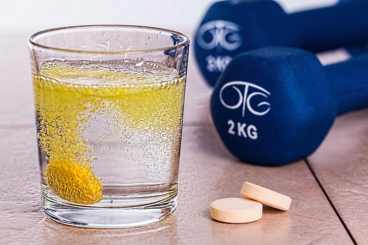 clear rock glass beside two white medication tablets near pair of 2 kg blue fixed dumbbells