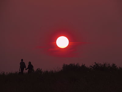 silhouette photography of two person walking on grass field during full moon