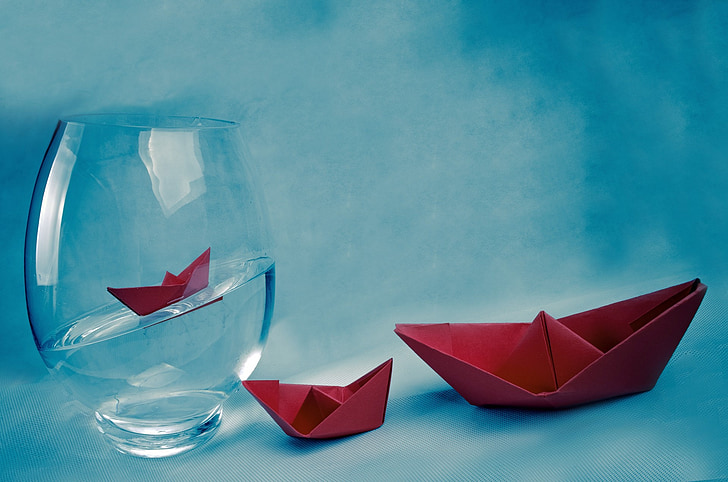 two red origami boats beside clear glass fish bowl filled with water