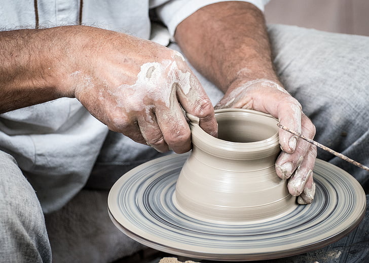 Royalty-Free photo: Person in gray shirt and gray pants molding clay pot