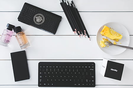 black wireless keyboard; plate with spoon; pencils; Versace wallet; two clear glass bottles