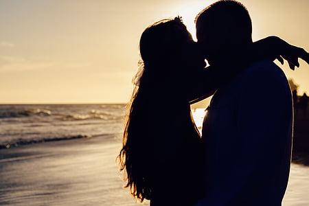 silhouette of man and woman kissing by the seashore during golden hour
