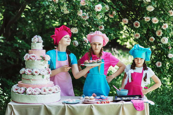 three girls baking cake near trees