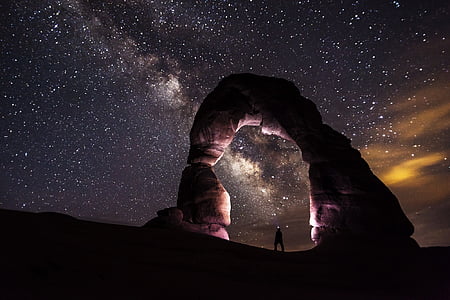 silhouette of man under formation of rock during nighttime
