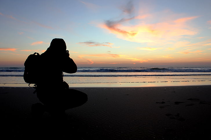 man capturing sunset on beach shore