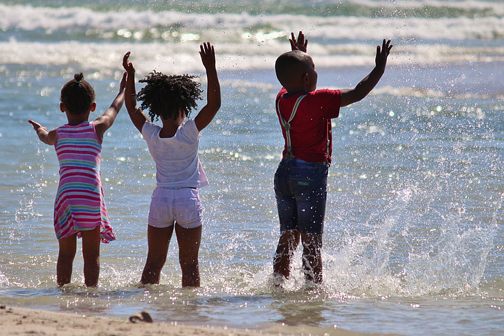 three kids playing on grey body of water during daytime