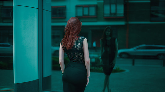 woman in black dress standing near black wall glass