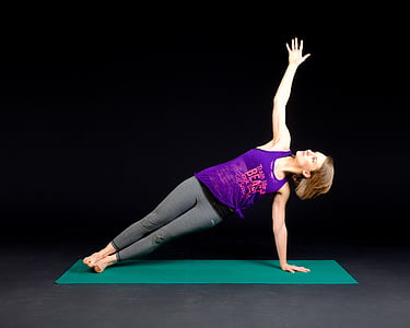 woman wearing purple tank top and gray leggings with and yoga position on green yoga mat
