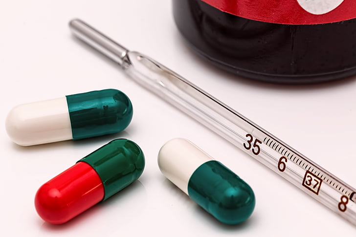 person taking photo of three medication capsules with thermometer