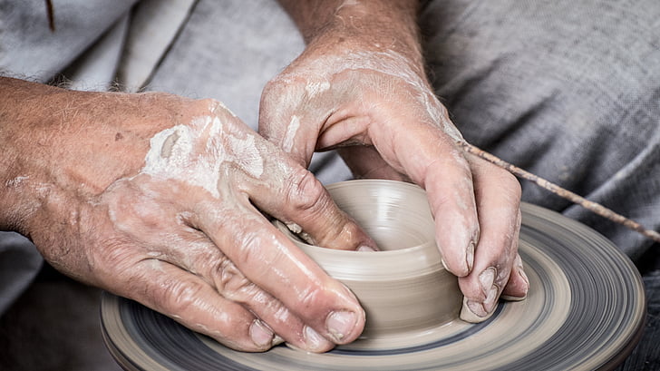 person molding gray clay pot