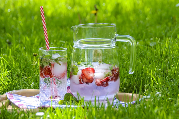 fruit juice in clear glass pitcher with drinking glass on green grass