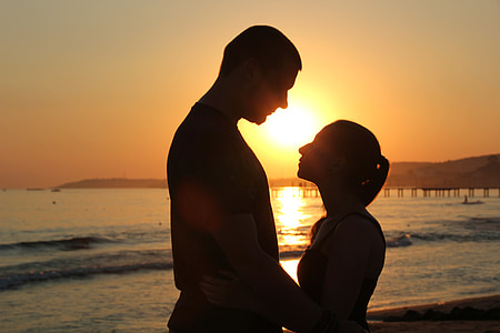 silhouette photo of man and woman standing near beach
