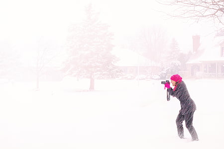 woman wearing black coat white holding camera in the middle of snow storm
