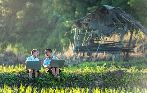 two toddlers sitting on grass field while holding gray laptops