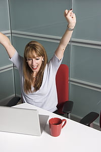 woman sitting on office chair front of laptop raising hands