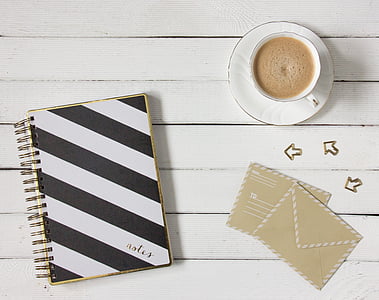 white and black striped notebook and white ceramic tea cup and saucer set