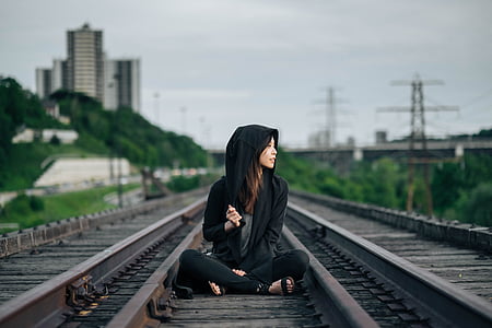 woman wearing black zip-up hooded jacket sitting on train railway