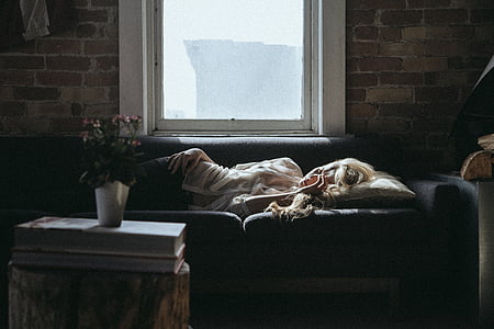 woman in white shirt sleeping on black couch near glass window with white frame during daytime