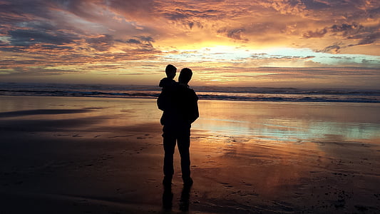silhouette of man carrying baby beside the seashore
