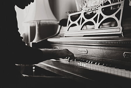 grayscale photo of person playing upright piano