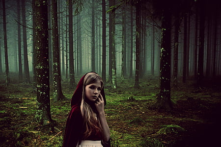 woman wearing red cloak standing in middle of forest