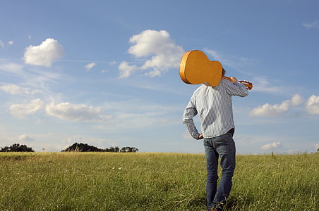 person holding guitar standing on green grass field
