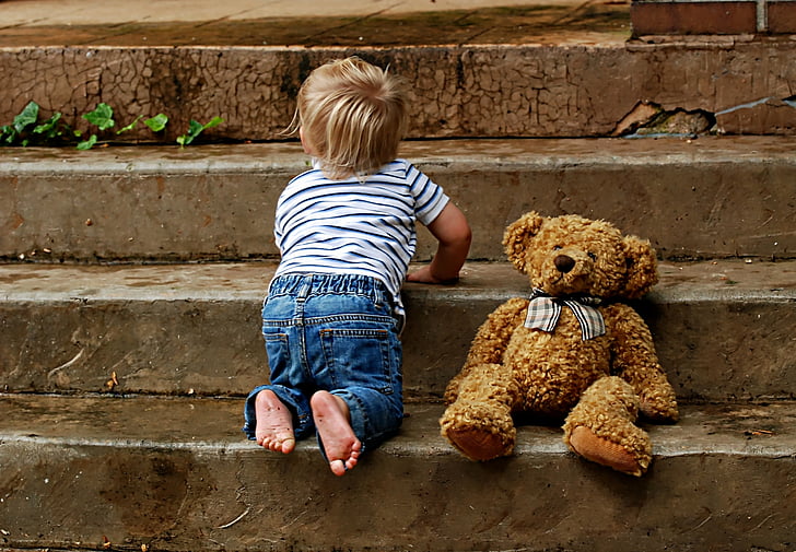 toddler beside brown bear plush toy climbing flight of stairs