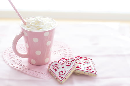 white ceramic mug filed with cream beside two heart-shaped cookies
