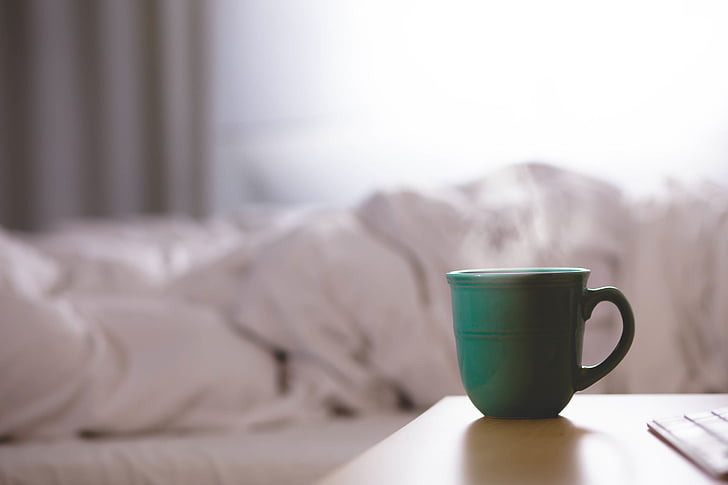 green teacup near white bed sheet