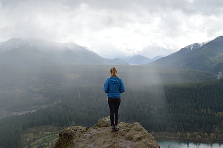 woman in blue hoodie and black bottoms standing on the edge of cliff