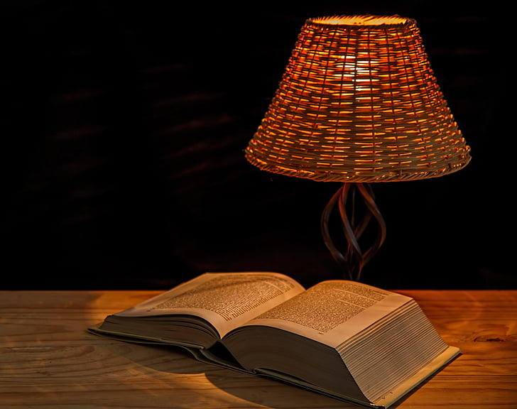opened book on table near turned on table lamp