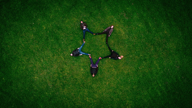 five people forming a star while lying on grass field