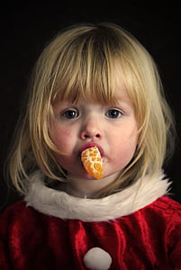 girl biting orange fruit wearing Santa costume